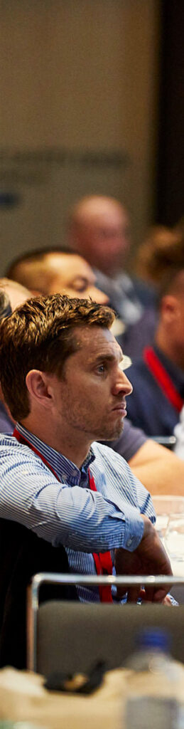 Man wearing stripped collar shirt at a conference watching speaker